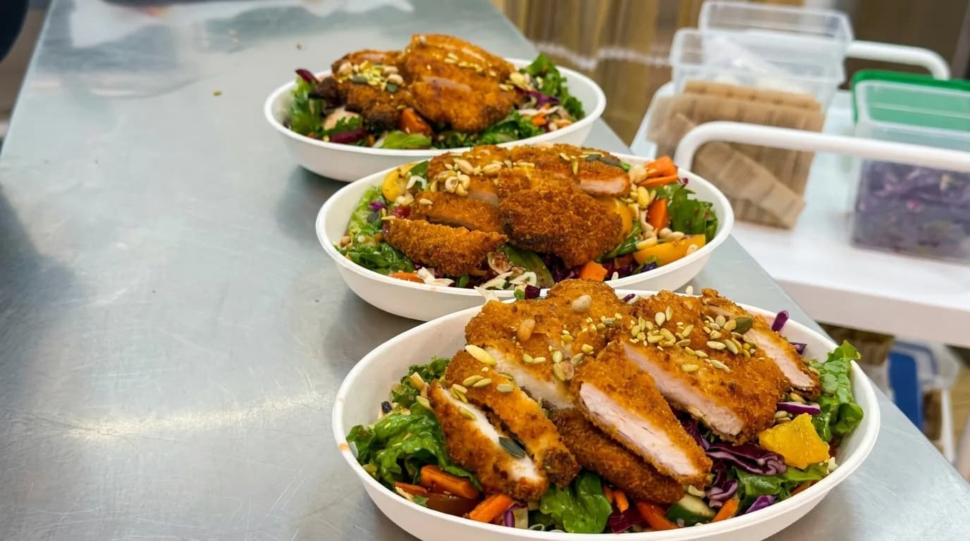 Prepared salad bowls topped with sliced breaded chicken at Moringa Cafe